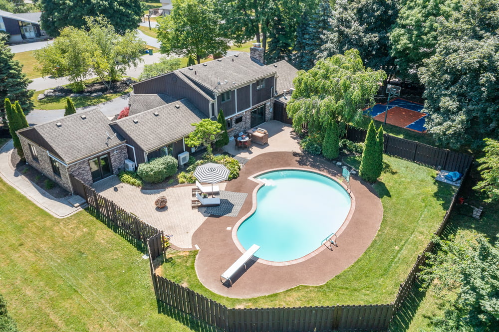 Drone shot of a home with a swimming pool in a fenced in backyard.
