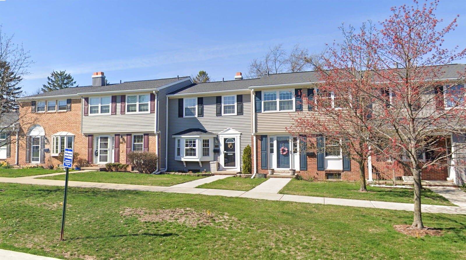 Exterior view of Highland Lakes Condo subdivision showing a row of two-story townhouses with brick facades and varying siding colors, manicured lawns, and a clear blue sky in the background